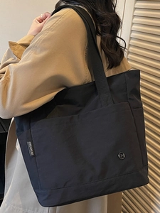 Black large capacity nylon tote bag shown on shoulder in a stylish minimalist setting