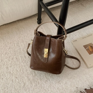 Détail du sac seau en cuir ciré marron avec boucle dorée et texture de cuir raffinée