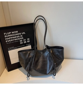 Detail of black soft leather tote bag with decorative drawstrings and silver buckle
