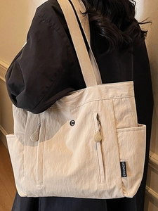 Minimalist beige tote bag with large capacity and double front zip pockets shown on shoulder