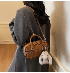 Sac Boston en daim marron avec breloque lapin porté sur un blazer en laine grise