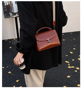 Detail of caramel leather crossbody bag with contrast stitching and woven strap