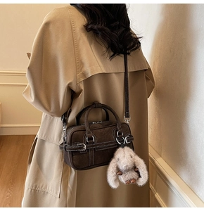 Détail du sac boston en daim marron foncé avec surpiqûres et pendentif lapin en peluche