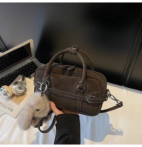 Détail du sac à main cylindrique en daim marron avec surpiqûres et breloque en fourrure de lapin