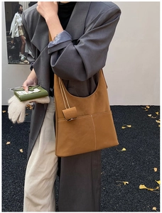 Close-up of brown suede shoulder bag with white stitching and decorative small pouch