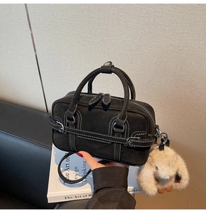 Détail du sac Boston noir en daim avec surpiqûres blanches et charme en peluche beige