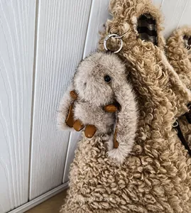 Close-up of a fluffy gray bunny charm attached to a beige teddy tote bag