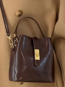 Sac seau vintage marron foncé avec fermoir doré porté sur un manteau en laine camel