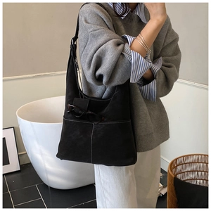 Detail of black suede tote bag with white contrast stitching shown on model shoulder