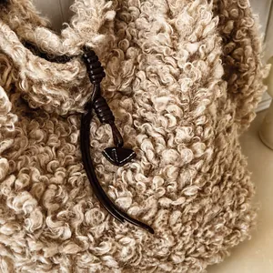 Detailed close-up of beige fuzzy faux shearling texture and brown braided cord on tote bag