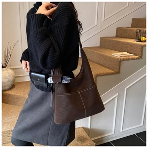Detail of dark brown suede tote bag with white stitching and mini charm on the strap
