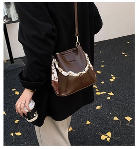 Detail of a brown bucket bag with a silk scarf chain on a street style model background