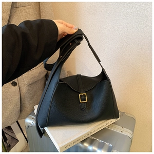 Détail du sac à main noir en cuir grainé avec boucle dorée posé sur une valise de voyage