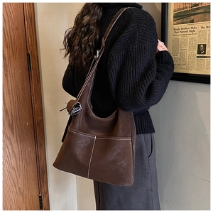 Detail of a brown leather tote bag with white contrast stitching and an outer pocket