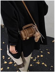Detailansicht einer braunen Boston-Zylindertasche mit Goldnieten und Bärenanhänger