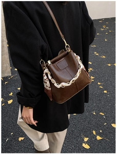 Close-up of brown bucket bag with gold chain and silk scarf detail on ginkgo leaf ground