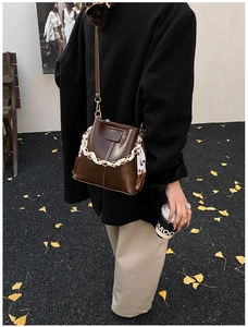 Detail view of deep brown bucket bag with silk scarf handle and gold chain accessory