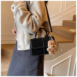 Detail of black tote bag with white contrast stitching and brown plush bear charm accessory