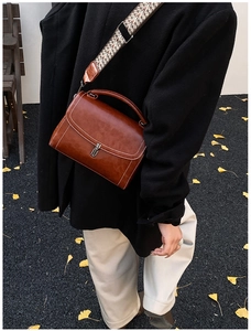 Close-up of brown PU leather handbag featuring white contrast stitching and silver metal lock