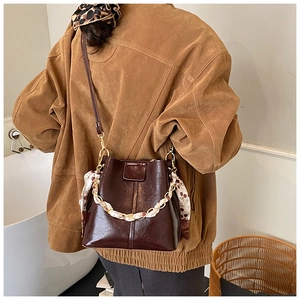 Close-up of dark brown bucket bag with shiny leather texture and silk scarf handle detail