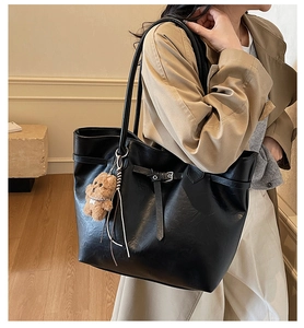 Detailed view of black leather tote bag with a cute brown plush bear charm accessory