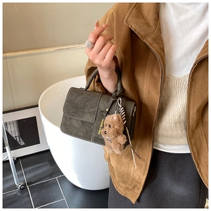 Detail of olive green leather handbag with a plush brown teddy bear charm and metal buckle