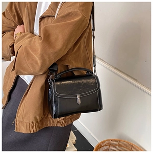 Detail view of black glossy leather crossbody bag featuring white contrast stitching and silver lock