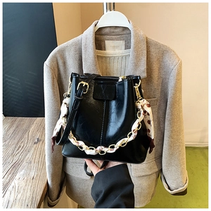 Detail of black glossy bucket bag featuring gold chain with elegant silk scarf wrap