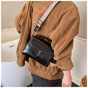 Detail of glossy black handbag with wide textured shoulder strap and silver hardware buckle