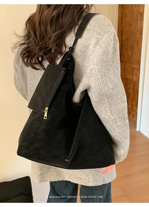 Minimalist large black suede tote bag with zipper pouch on a model in a warm interior