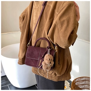 Detail of wine red matte crossbody bag with contrast stitching and plush dog charm