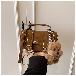 Detail einer braunen Boston-Tasche mit goldenen Perlen und einem Plüsch-Hundeanhänger