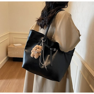 Detail of a black leather tote bag with side strap and a brown plush bear charm