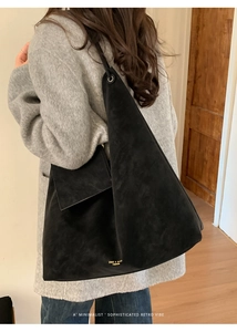 Detail of a large black triangular tote bag made of matte suede fabric with gold branding