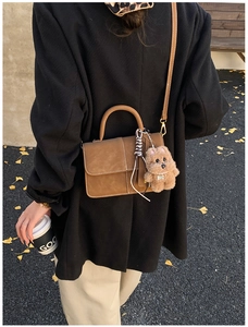 Brown suede crossbody bag detail with plush dog charm and stitching on golden autumn leaves