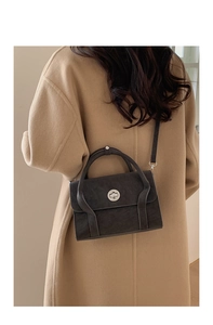 Detail of dark brown vintage shoulder bag with metal turn-lock on wool coat