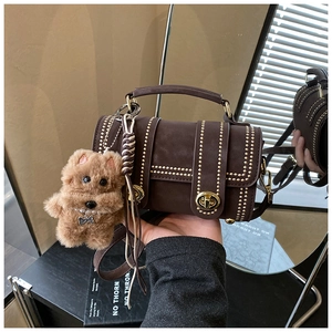 Detail der braunen Vintage-Zylindertasche mit Goldnieten und Plüschbär-Anhänger