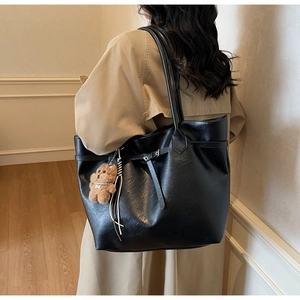 Large black tote bag with tassel detail and plush bear charm shown on a model