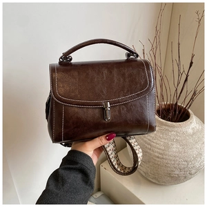 Detail of dark brown leather handbag featuring houndstooth strap and metal buckle closure
