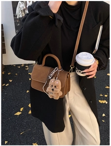 Close-up of brown suede handbag with golden hardware and cute plush charm detail