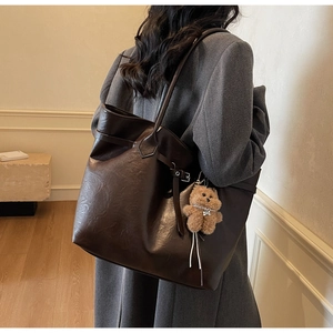 Detail view of large dark brown tote bag with leather straps and plush bear charm