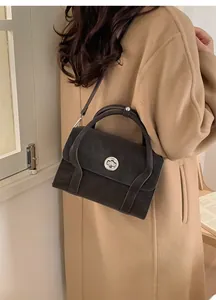 Detailed close-up of dark grey suede crossbody bag with round silver buckle and slim strap