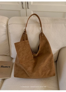 Detail of caramel suede hobo bag with matching zipper pouch on a soft cream sofa
