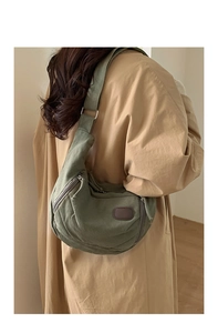 Detailed view of an olive green canvas crescent bag worn with a khaki coat