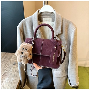 Detail view of burgundy frosted shoulder bag with white stitching and plush puppy pendant
