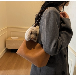 Detail of brown faux leather shoulder bag with a plush bunny charm and adjustable strap