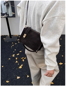 Close-up of dark brown suede shoulder bag featuring a gold metal buckle and pebble background