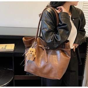Brown leather tote bag with teddy bear charm shown from 45-degree angle