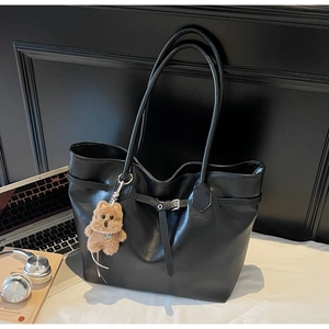 Detailed view of a large black leather tote bag with a brown plush bear and laptop
