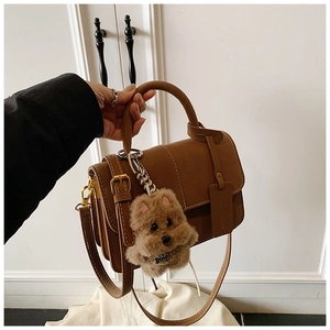 Detail view of brown vintage leather crossbody bag with cute plush dog charm accessory